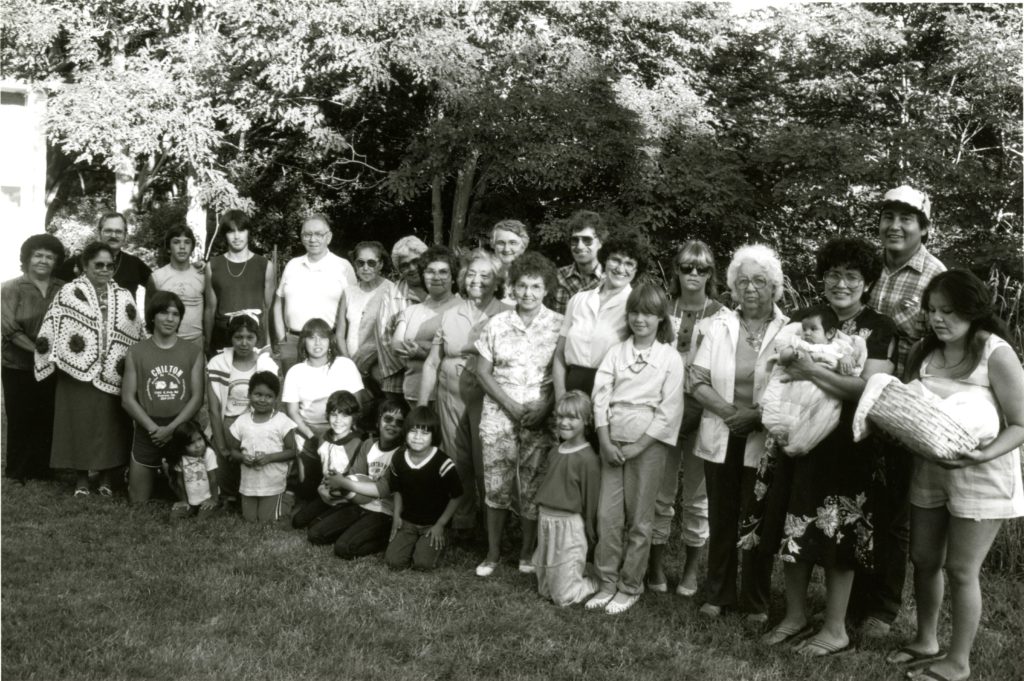 A Lummi group of around 20 people from multiple generations poses for a picture beneath a tree.